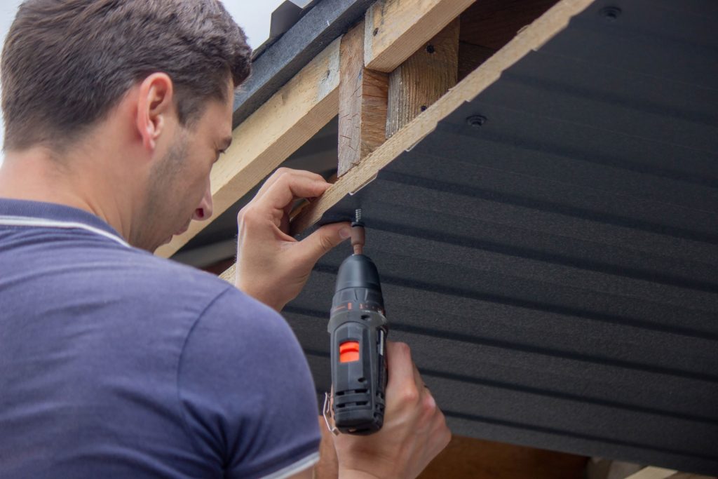 Man repairing a roof with a power drill, focusing on roof maintenance and preventative measures for homeowners in Redding, California.