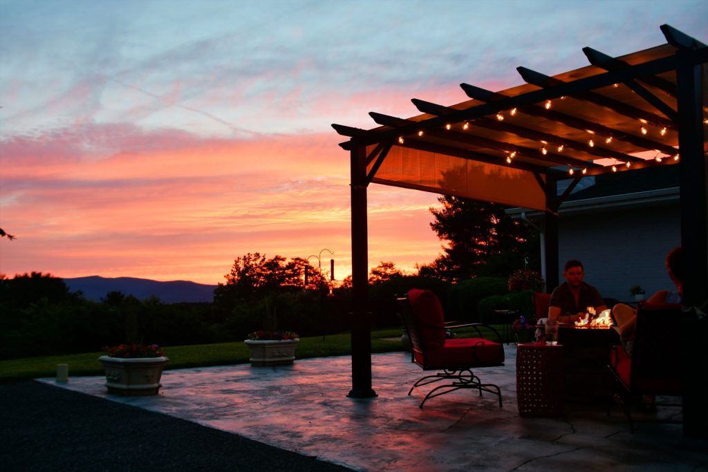 Family gathered around a fire pit under a stylish patio cover, enjoying a sunset view with warm lighting and a serene outdoor ambiance.