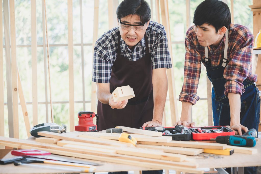 Professional carpenters discussing project details over a workbench filled with tools and wooden materials, emphasizing craftsmanship and quality in home remodeling.