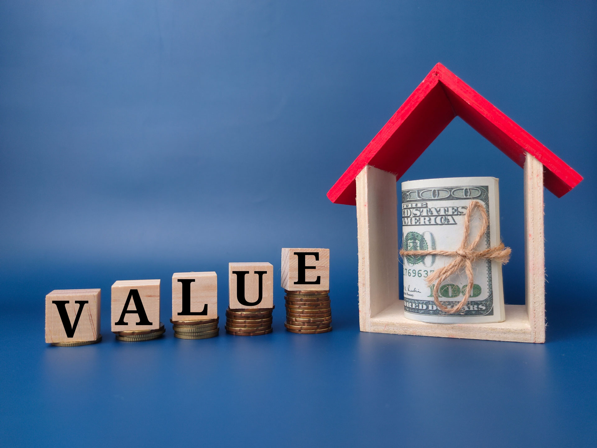Toy house and bank note with the word VALUE beside it.