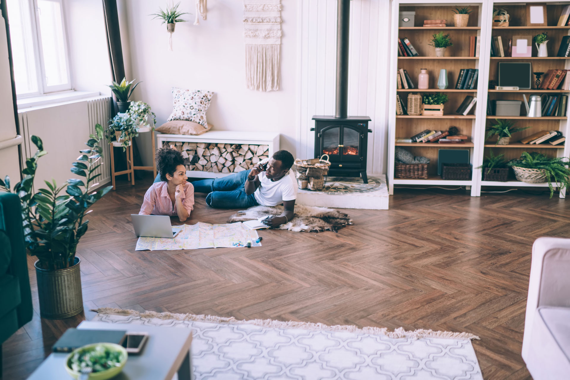 Woman in a laptop lying on floor with her boyfriend talking on the phone.
