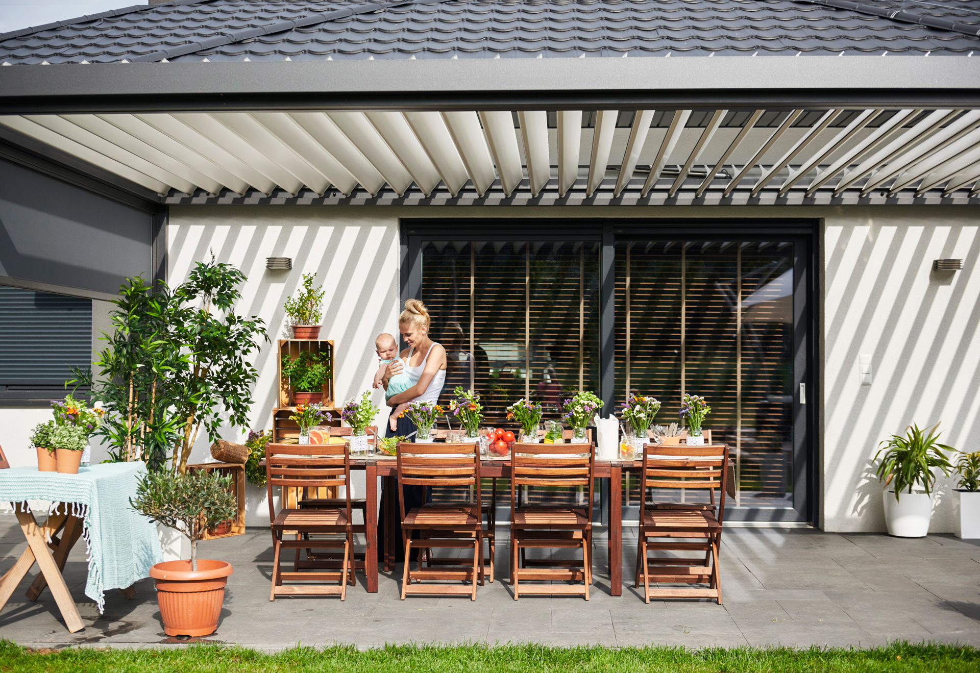 Woman holding baby outdoor under a pergola.